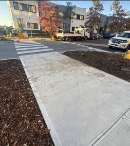 Screenshot | PROCons Construction scene at a city intersection: a work truck parked by fresh crosswalk paint, orange cones, and signs, with apartment buildings in the background.