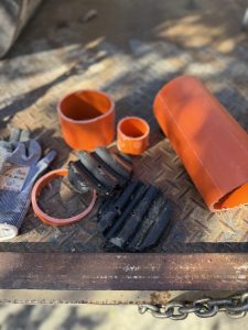 IMG_6992 | PROCons Orange PVC pipe sections and black straps on a rusted diamond-plate surface, with a chain in the foreground, suggesting construction debris.
