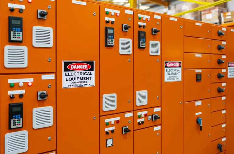Row of orange industrial switchboard cabinets with control switches, indicator lights and electrical hazard signage